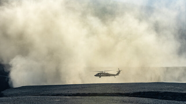 Silhouette of military Black Hawk helicopter landing or taking off in a dust cloud