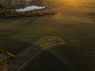 Aerial view with beautiful cereal field at sunset with a huge stone house in the middle of the field. The building resembles stonehenge. Smiltene stonehenge, Latvia