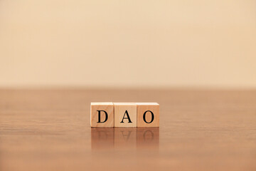 DAOの文字。分散型自律組織。3つの木製ブロックに書かれている。黒い文字。木製テーブルの背景。