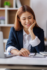 Asian Business woman using calculator and laptop for doing math finance on an office desk, tax, report, accounting, statistics, and analytical research concept