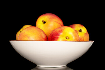 Several sweet organic nectarines on a ceramic plate, close-up isolated on a black background.