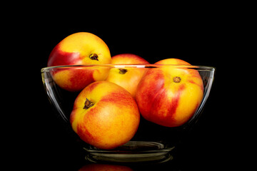 Several sweet organic nectarines in a glass bowl, close-up isolated on a black background.
