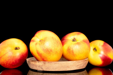 Several sweet organic nectarines on a wooden saucer, close-up isolated on a black background.