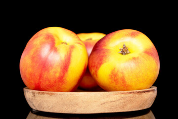 Three sweet organic nectarines on a wooden saucer, close-up isolated on a black background.