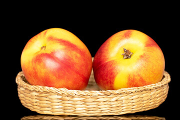 Two sweet organic nectarines on a straw dish, close-up isolated on a black background.