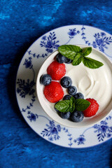 Natural yoghurt bowl close up photo. Sweet breakfast on blue stone table. Strawberry, blueberry, cherry, mint leaves on Greek yogurt. Eating healthy concept. 