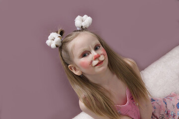 A girl with blue eyes and children's makeup. A child with a funny face painting. Makeup of a rabbit on the face of a child. Children's holiday, event, birthday, easter bunny, entertainment