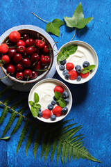 Non dairy yogurt with organic strawberry, blueberry, cherry and mint leaves. Healthy vegetarian breakfast on a table. Top view photo of fresh summer fruit. 