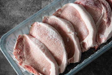 Frozen pork chops in plastic tray packaging thawing.  On a concrete background