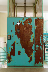 The door of a very old elevator with peeling blue paint and traces of rust