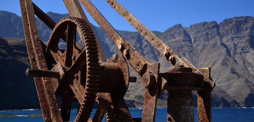 Fototapeta premium Old rusty crane by the sea, old dock of Agaete, coast of Gran Canaria, Spain