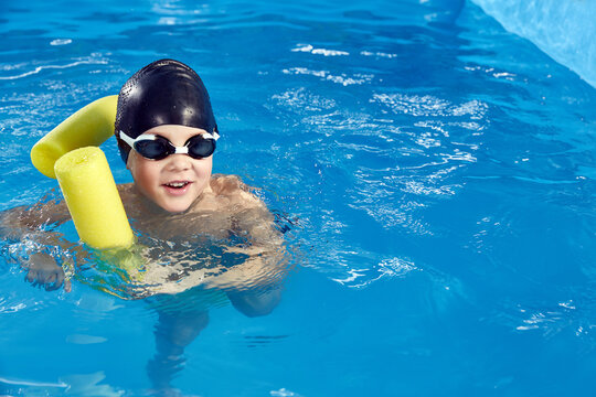 Preschool boy learning to swim in pool with foam noodle