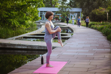 An old slender woman does yoga in the park