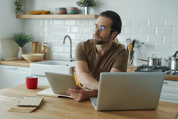 Confident young man using technologies while working at the kitchen island at home