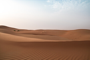 Landscape of sand dunes against a bright blue sky in Al Wathbah Desert in Abu Dhabi, United Arab Emirates.
