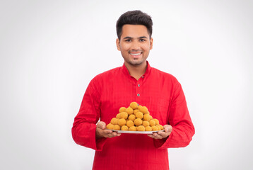 Indian man holding plate full of laddoos against white background