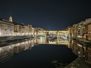 Night photo of the Arno river, in the stretch crossed by the Ponte Vecchio which is reflected in the calm water.
