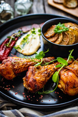 Barbecued chicken drumsticks with fried potato on wooden table
