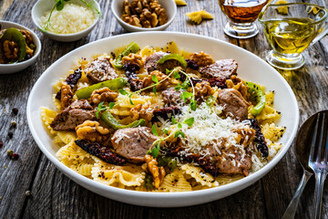 Farfalle with roasted pork loin, sauce, parmesan cheese, nuts and  green bell pepper served on wooden table
