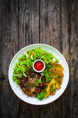Roasted pork loin and fried potatoes with green vegetables  on wooden table
