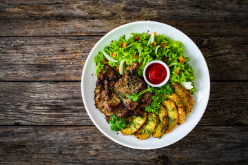 Roasted pork loin and fried potatoes with green vegetables  on wooden table
