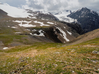 Summer view from sunlitgreen rocky slope to a narrow mountain gorge under cloudy sky. Colorful...