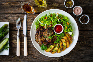 Roasted pork loin and fried potatoes with green vegetables  on wooden table
