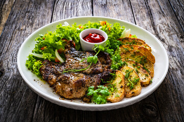 Roasted pork loin and fried potatoes with green vegetables  on wooden table
