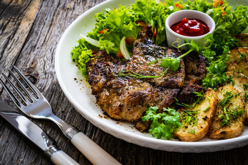 Roasted pork loin and fried potatoes with green vegetables  on wooden table
