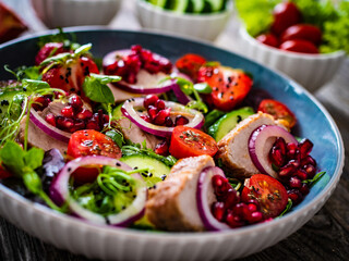 Tasty salad - roast pork loin, cucumber, cherry tomatoes, pomegranate, strawberries and fresh, green vegetables on wooden table
