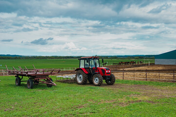 Red tractor in a rural landscape. Hay harvesting in the field by means of a tractor. Tractor against the sky with clouds