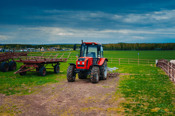 Red tractor in a rural landscape. Hay harvesting in the field by means of a tractor. Tractor against the sky with clouds