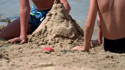 Children in swimsuits play in the sand on the beach. Little children build sand castles on the seashore. Children's entertainment at sea.