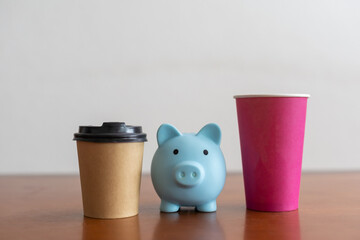 Levitating craft coffee cup with biggy bank on blue background.