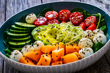 Fresh salad - mozzarella, melon and vegetables on wooden table
