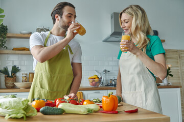 Happy couple drinking orange juice and smiling while cooking at the kitchen together