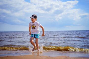 Happy little boy is running in the sea on sunny summer day. Childhood concept