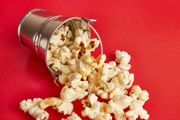 A small bucket filled with popcorn on a red background.