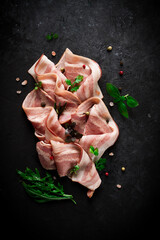 Raw bacon, sliced, with micro greenery and spices, on a black background, close-up,