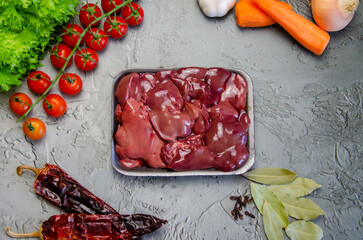Raw chicken liver, vegetables and spices for making pate on a textured concrete-gray background.