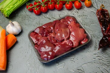 Raw chicken liver, vegetables and spices for making pate on a textured concrete-gray background.