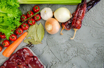 Raw chicken liver, vegetables and spices for making pate on a textured concrete-gray background.