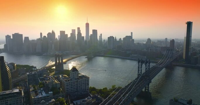 New York in the last rays of setting sun. Brooklyn and Manhattan bridges over East River with boat sailing along. Aerial view.