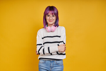 Cheerful young woman with headphones looking at camera while standing against yellow background