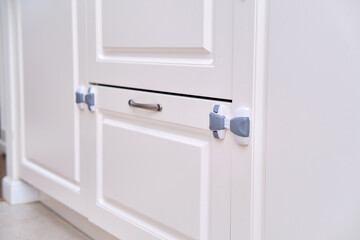 Doors of white cabinets blocked from children, no people. Lock furniture drawers from toddler baby, nobody