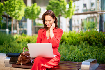 Confident businesswoman using laptop while sitting on the bench outside