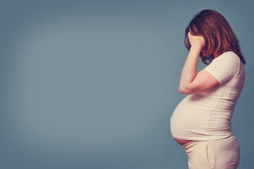 Headache problems during pregnancy in women, studio blue background, copy space with a place under...