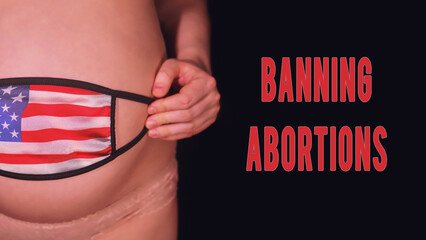 Inscription banning abortion and pregnant woman on black background with medical mask and usa flag....