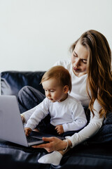 Young smiling freelancer mother pointing at laptop while holding little son