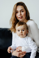 Son and mom sitting on couch at home and embracing celebrating mothers day looking at camera.